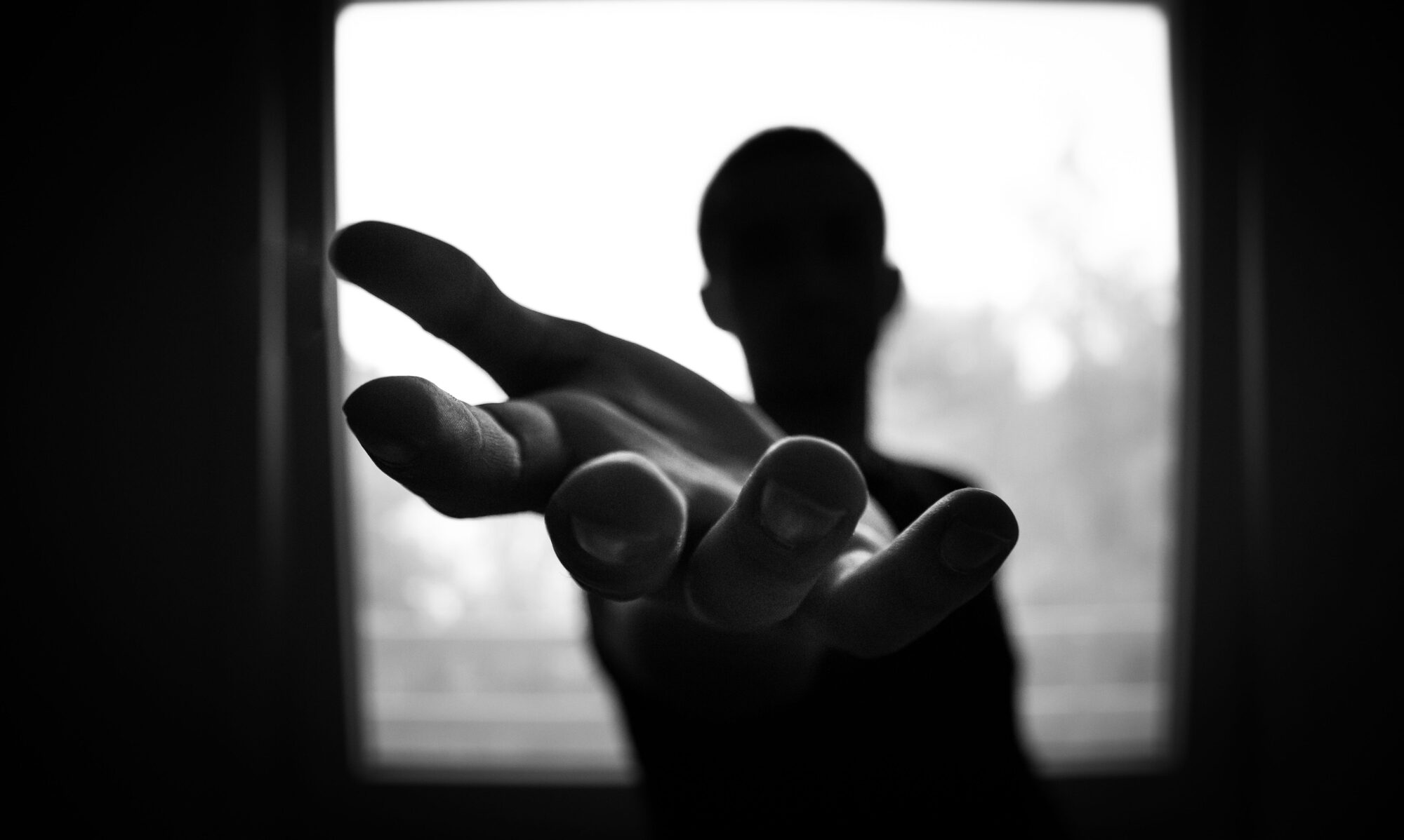 Mood still: a hand reaching toward window light.