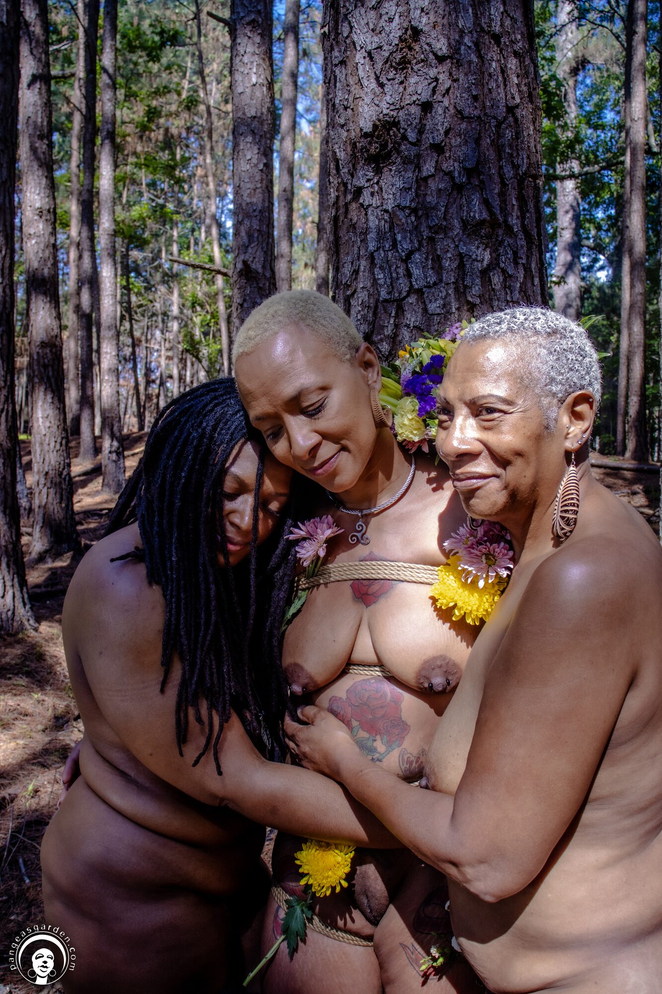 Three women embraced at the base of a pine, flowers tucked into the rope around them.